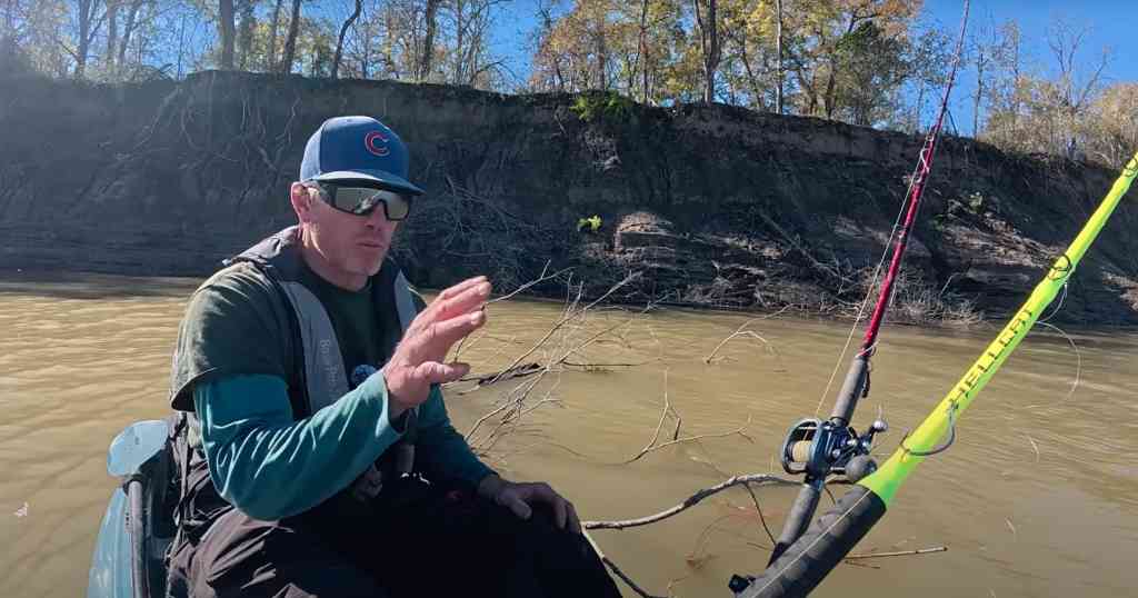 Spencer Bauer sits in his kayak along a muddy riverbank, preparing his Hellcat rod for winter catfishing.